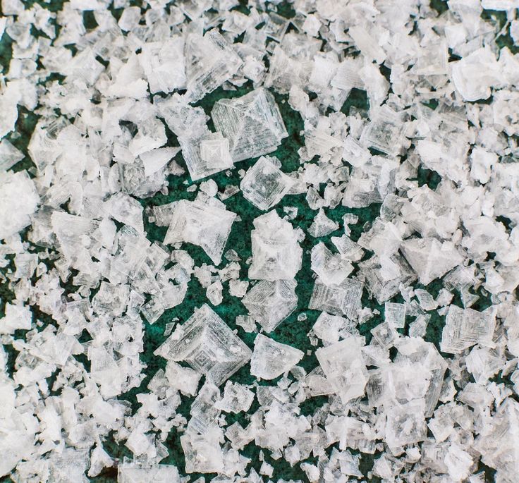 Pyramid flake salt crystals scattered across a deep green surface